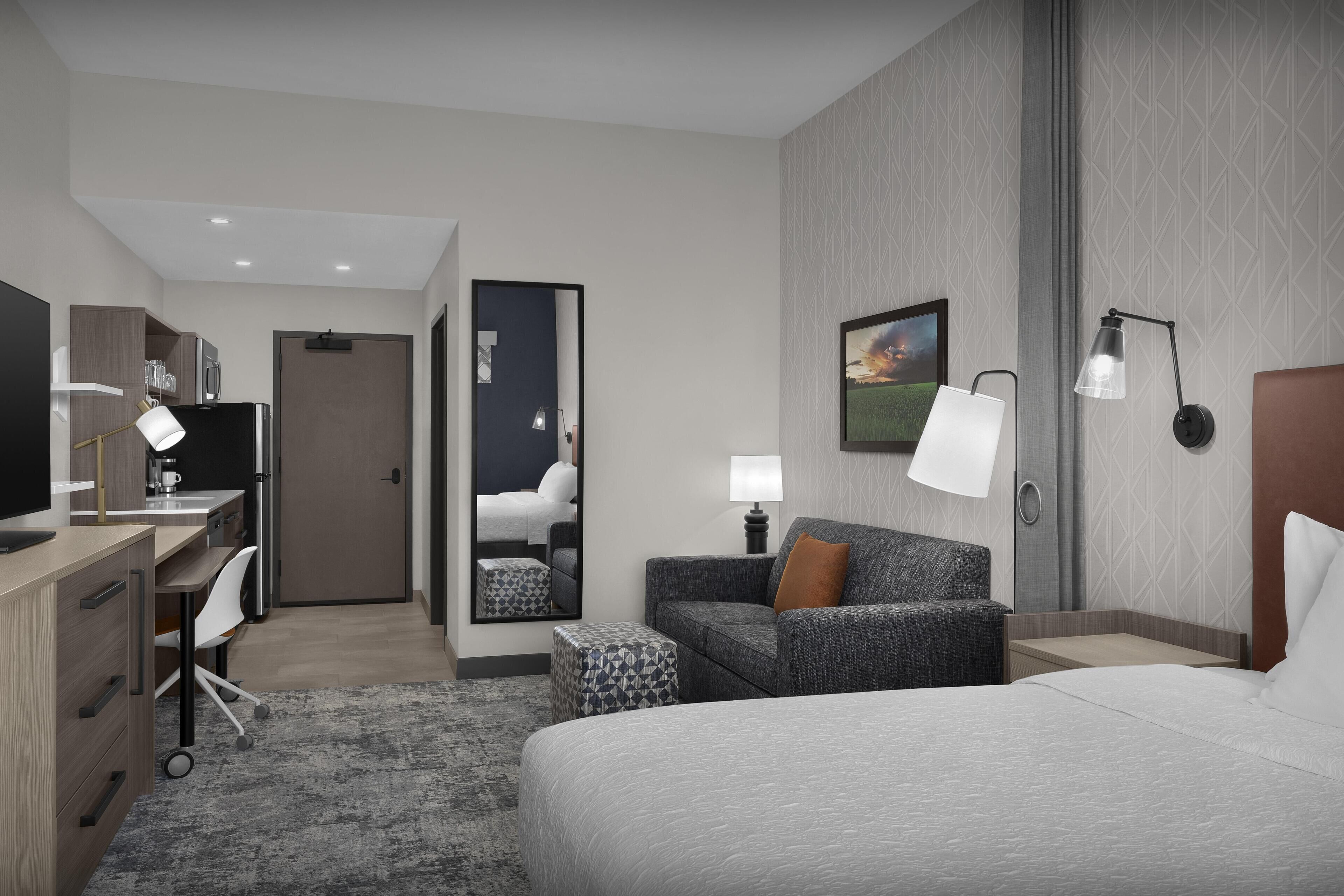 Una habitación de hotel moderna con cama, escritorio, silla y sofá.