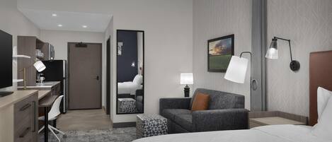 Una habitación de hotel moderna con cama, escritorio, silla y sofá.