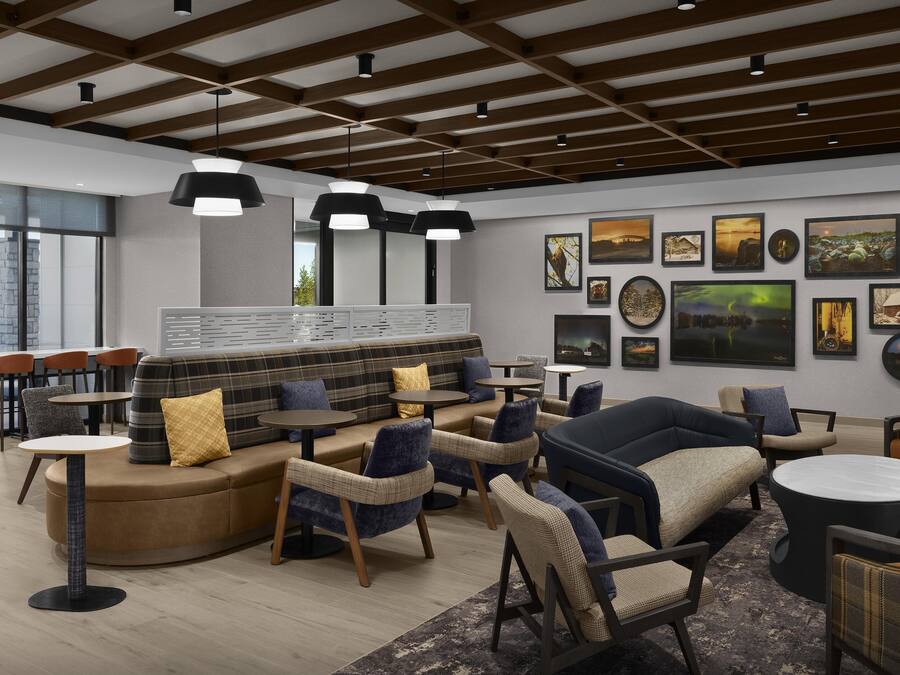 A modern lounge area with a sofa, armchairs, and tables, featuring a wooden ceiling and artwork on the walls.