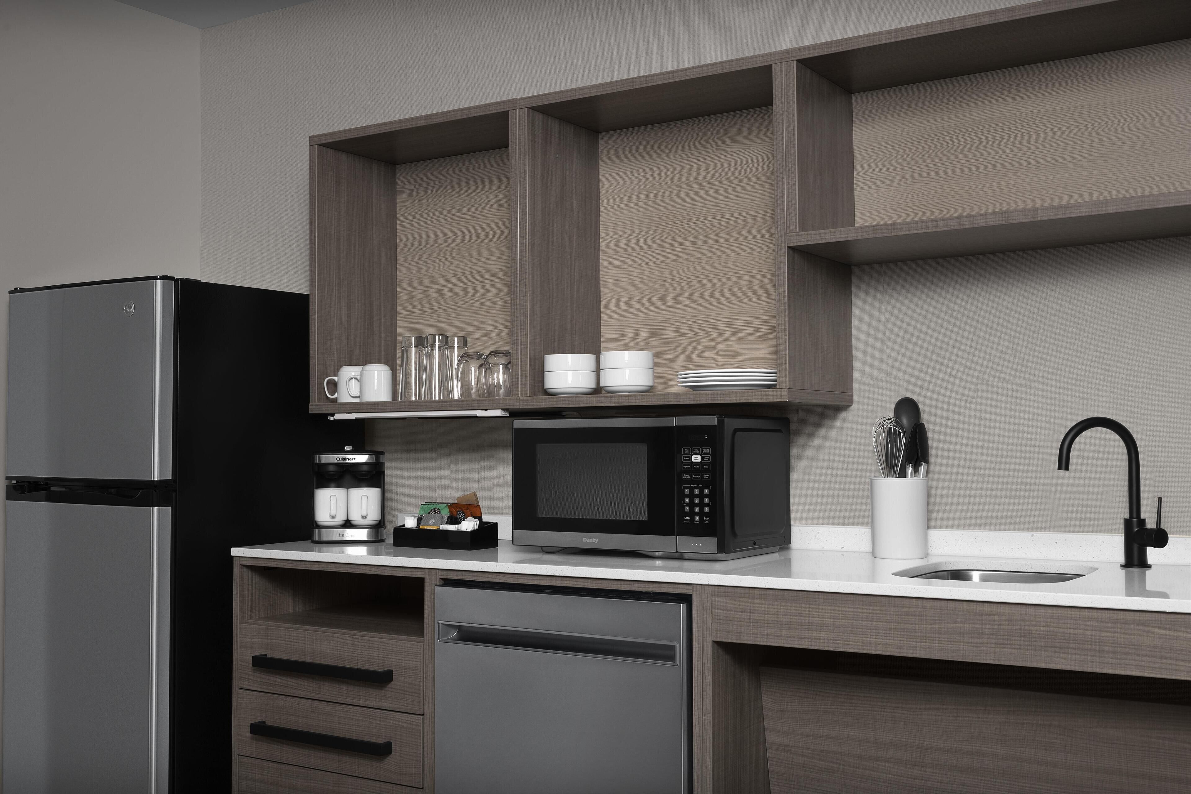 A modern kitchen with a stainless steel refrigerator, a black microwave, and a built-in dishwasher.