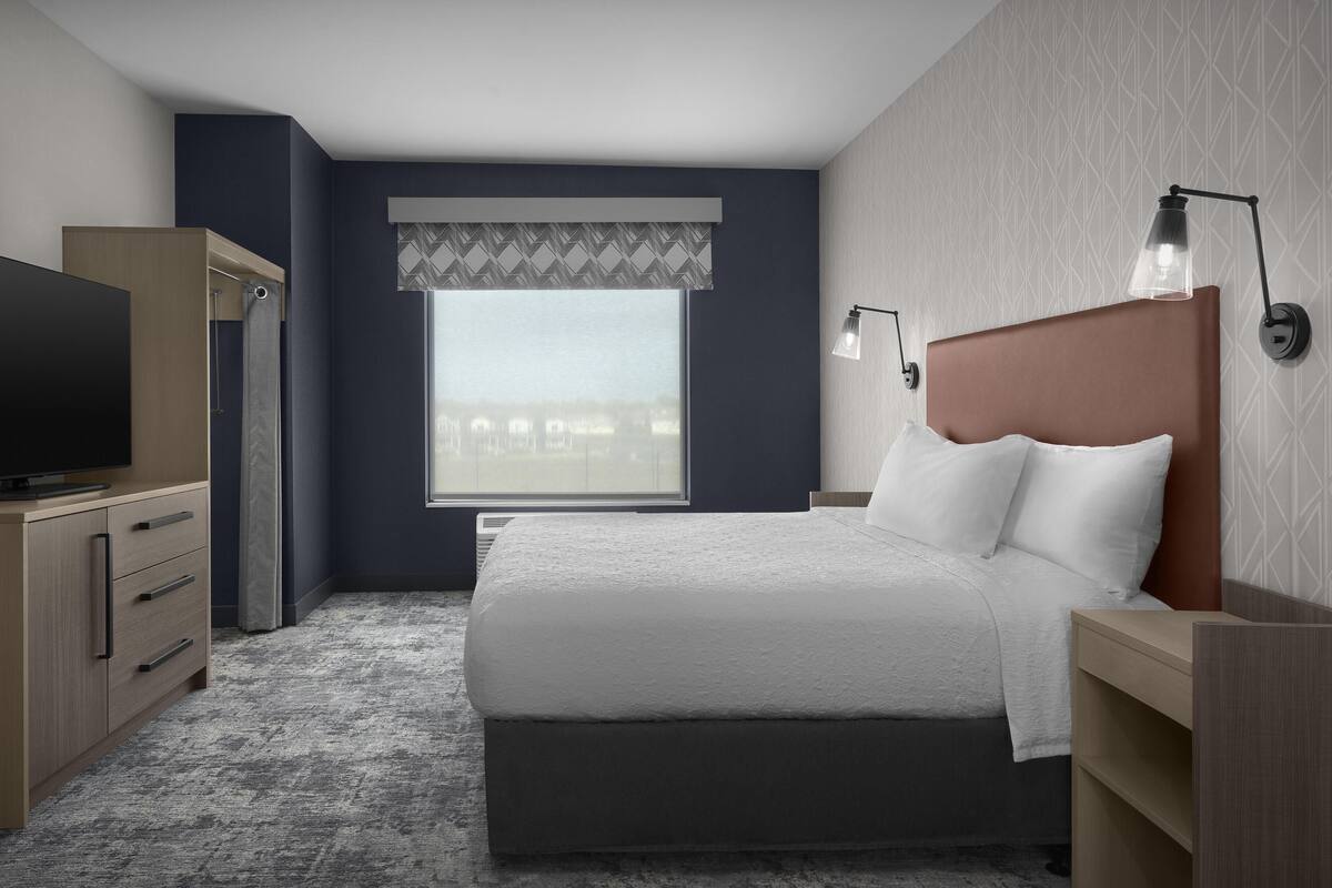 Una habitación de hotel moderna con una cama grande, televisión, armario y ventana con vistas a edificios.