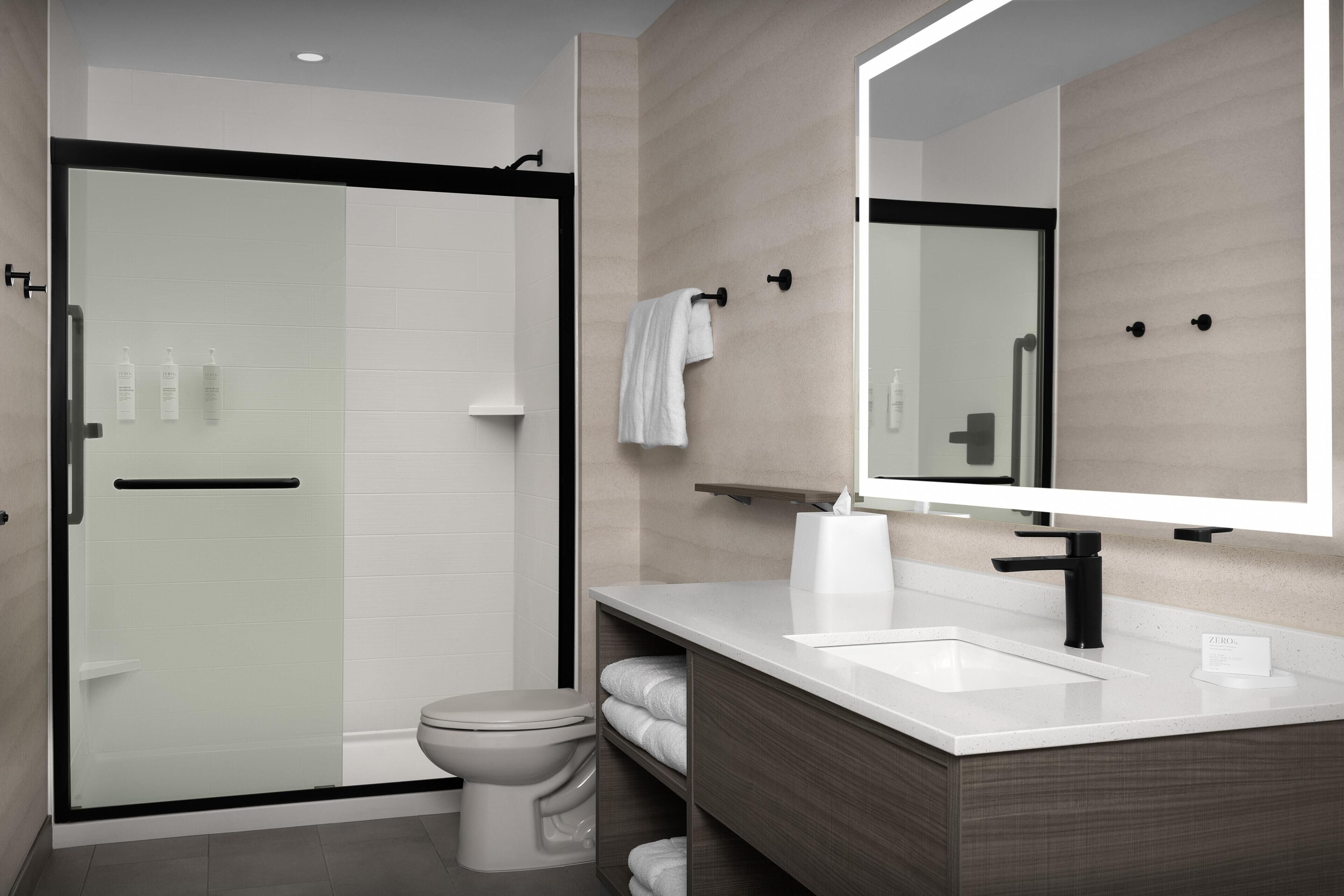 A modern bathroom with a glass-enclosed shower, a white toilet, and a vanity with a mirror.