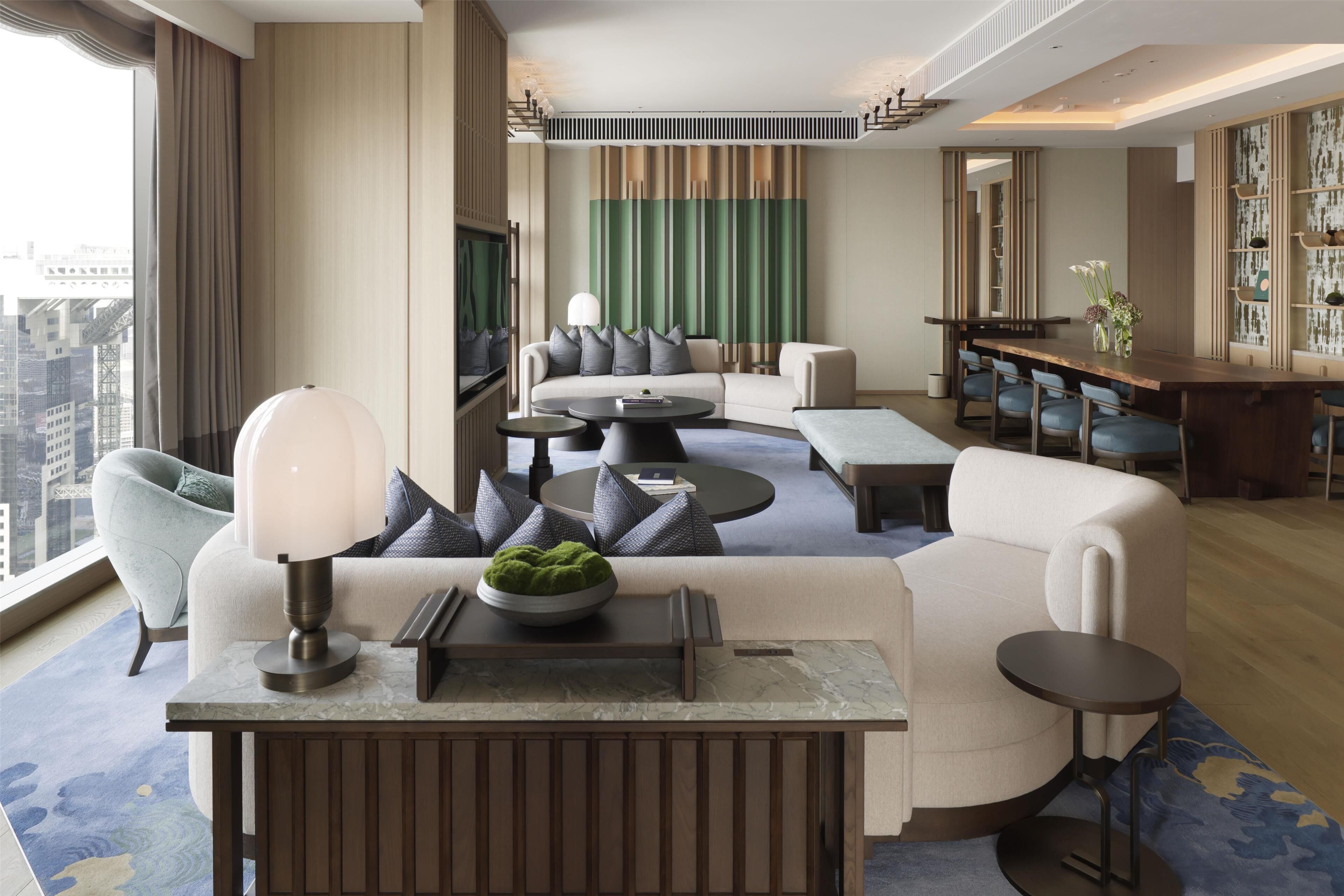A modern hotel lobby with a seating area, a bar, and a large window offering a city view.
