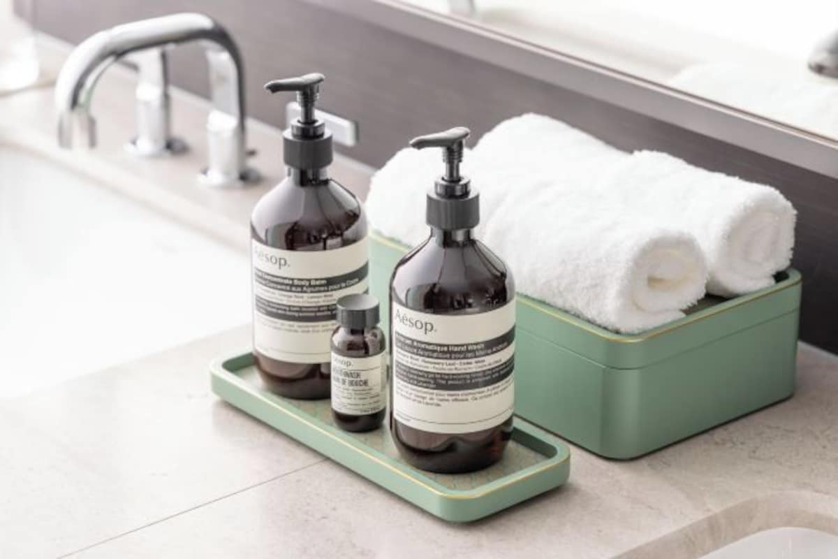A bathroom with a green tray holding two bottles of Aesop hand wash and a white towel.