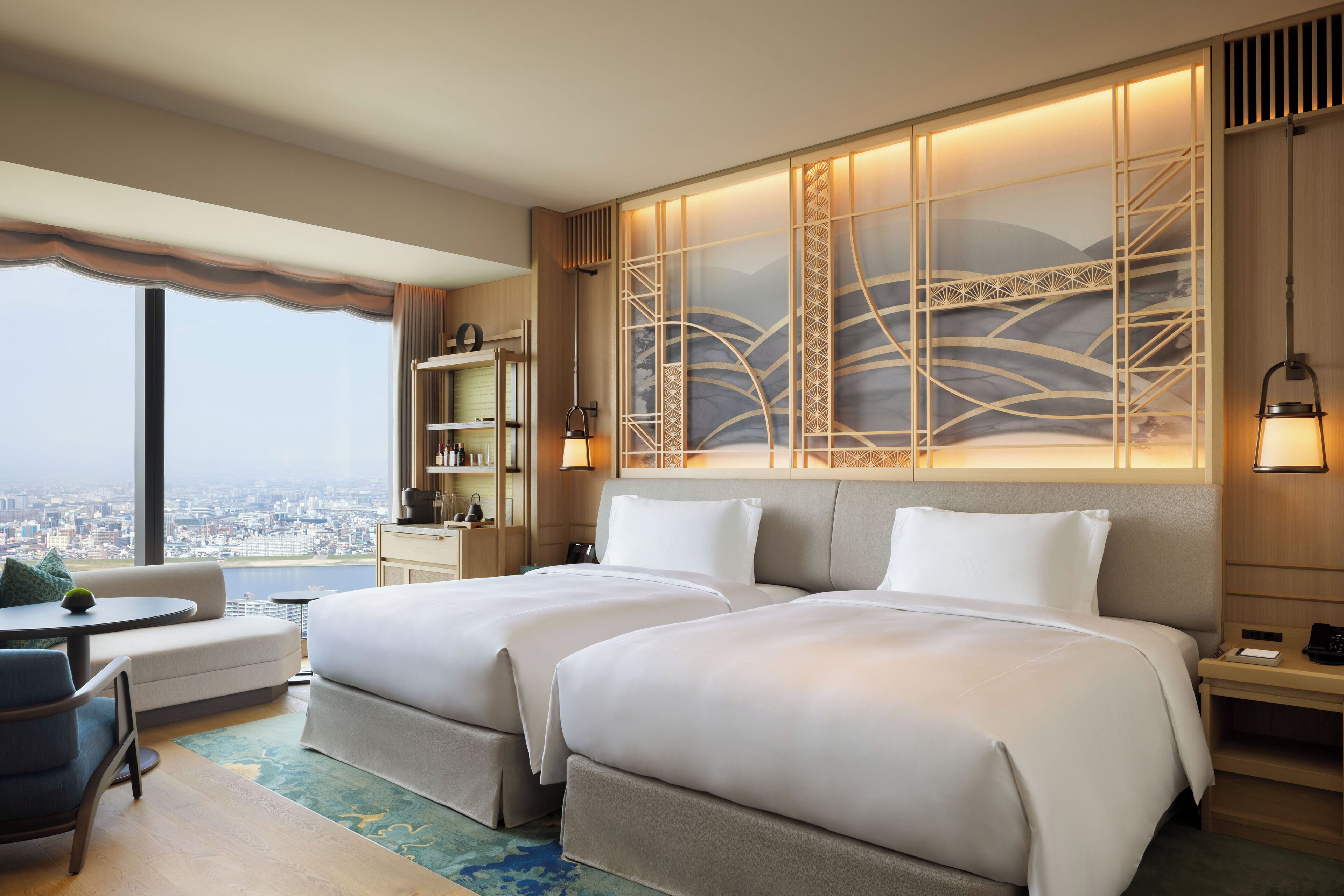 A hotel room with two beds, a sofa, a small table, and a view of the city.