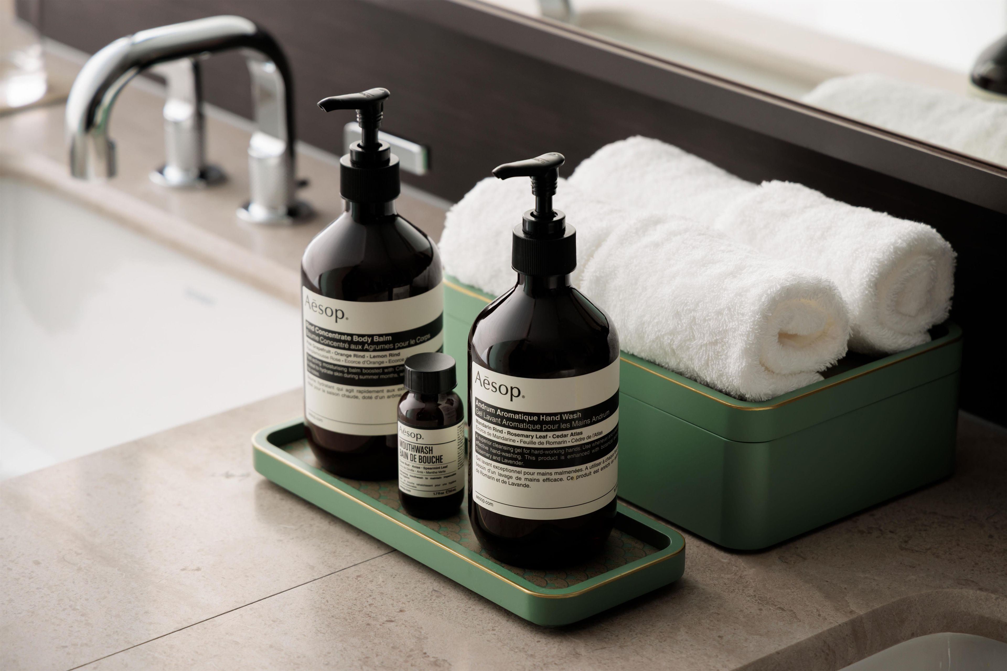 A bathroom with a green soap dish holding two bottles of Aesop hand wash and a green soap dish with a white towel.