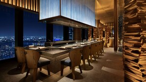 A modern dining area with a long table, wooden chairs, and a city view at night. - Waldorf Astoria Osaka (Osaka)