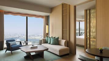 Habitación de hotel moderna con sofá, sillón, mesa de centro y vista a la ciudad.