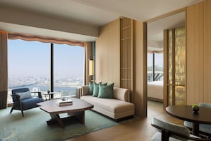 A modern hotel room with a sofa, armchair, coffee table, and a view of the city. - Waldorf Astoria Osaka (Osaka)