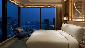 A hotel room with a large bed, a chair, a small table, and a view of a cityscape at night. - Waldorf Astoria Osaka (Osaka)