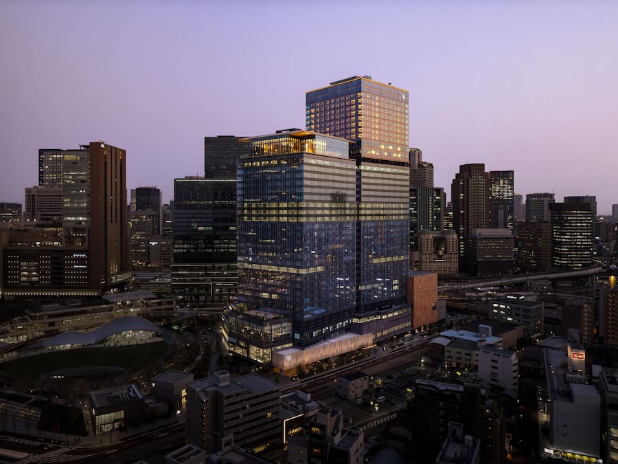 Um edifício alto com fachada de vidro, rodeado por outros arranha-céus em um panorama urbano.