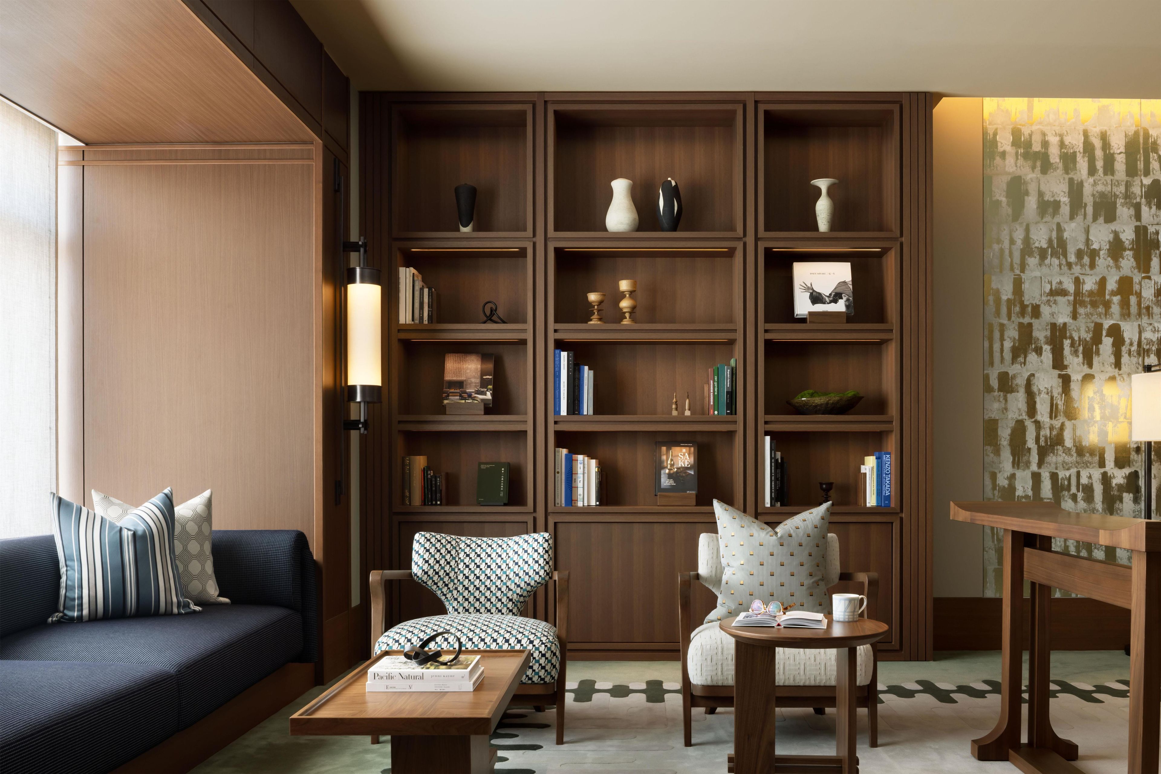 A modern living room with a dark blue sofa, patterned armchairs, a wooden coffee table, and a bookshelf filled with books and decorative items.