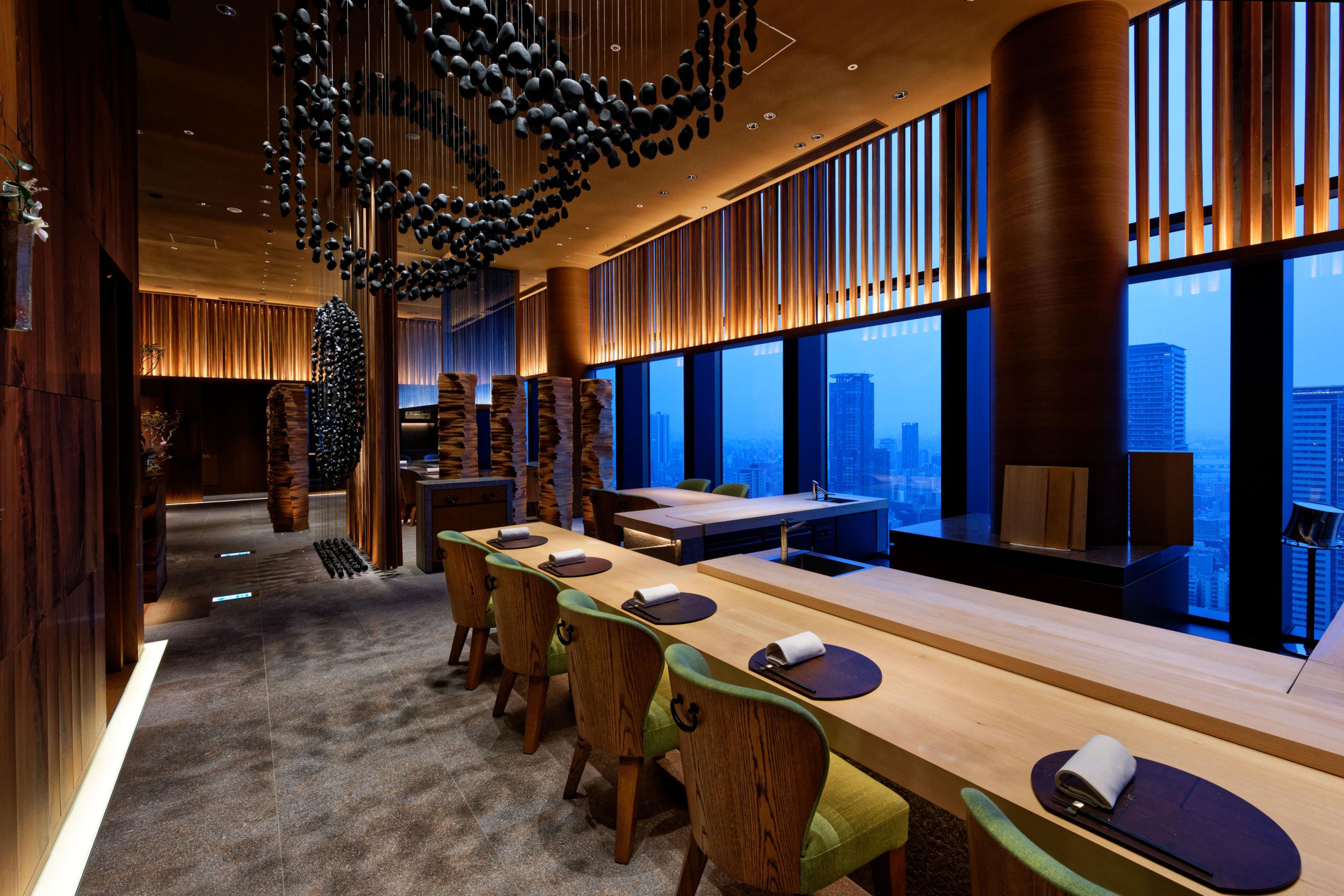 A modern hotel lobby with a long reception desk, seating area, and large windows offering city views.