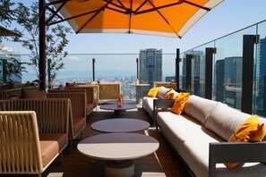 Um terraço com área de estar ao ar livre, um guarda-sol grande e vista para a cidade.