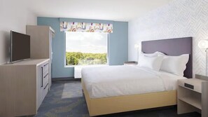 A hotel room with a bed, a TV, a desk, and a window with a view of greenery. - Home2 Suites By Hilton Springfield (Springfield)