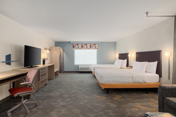 A hotel room with a bed, desk, chair, television, and a window with a patterned curtain.
