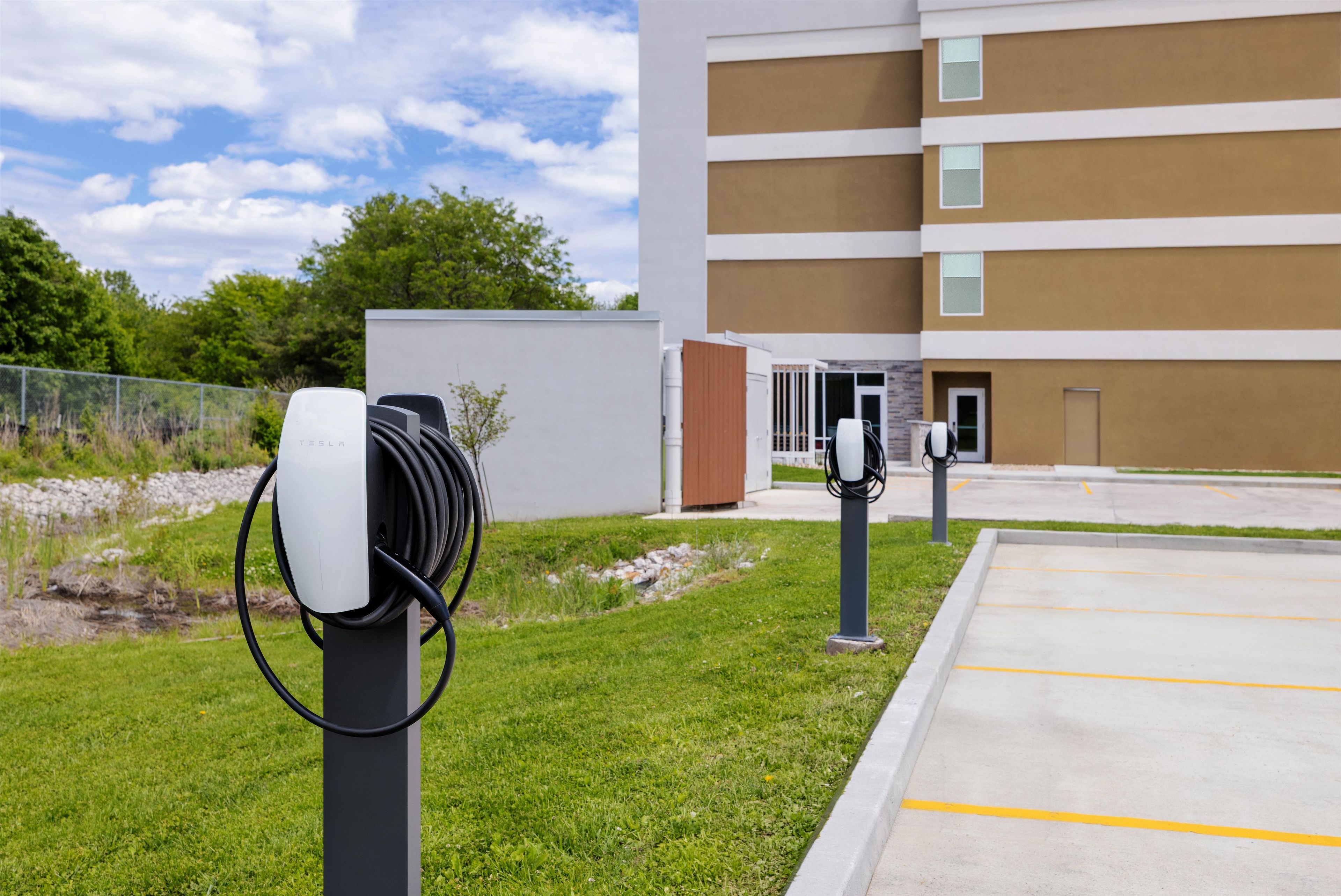 A parking area with electric vehicle charging stations, a grassy area, and a multi-story building in the background.