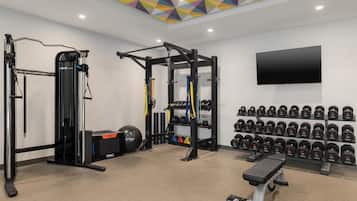 A gym with weightlifting equipment, a bench, and a wall-mounted TV.