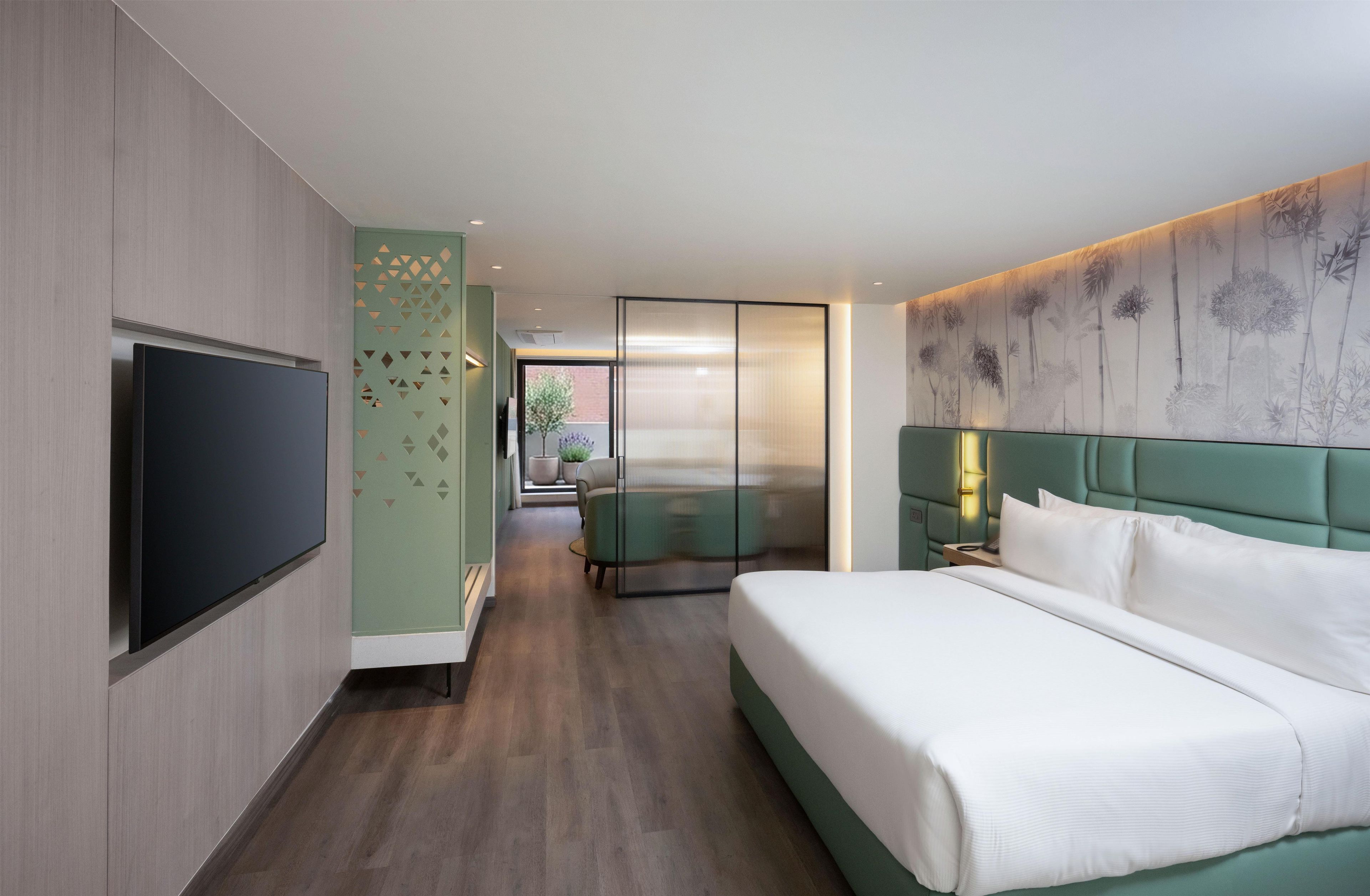 A hotel room with a bed, a TV, a seating area, and a view of the outdoors.