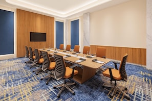 Une salle de conférence avec une longue table, de nombreuses chaises, un téléviseur à écran plat et une moquette à motifs.