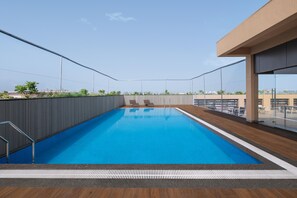 Une piscine sur le toit, avec une eau d’un bleu cristallin, entourée d’une terrasse en bois et de rampes en métal.