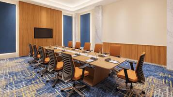 Une salle de conférence avec une longue table, des chaises, un téléviseur à écran plat et une moquette à motifs.