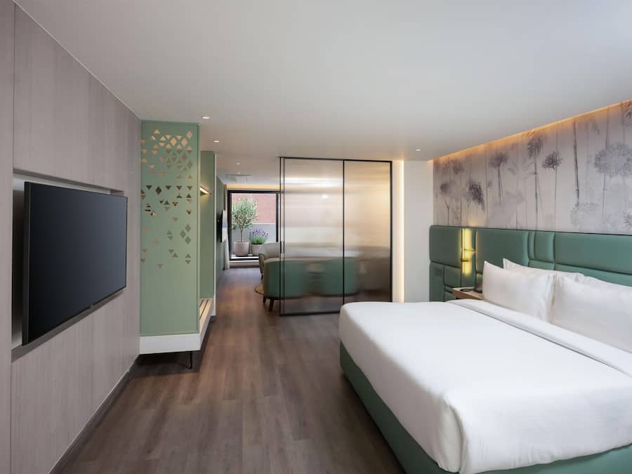 Ein Hotelzimmer mit Bett, Fernseher, Sitzecke und Blick ins Freie.
