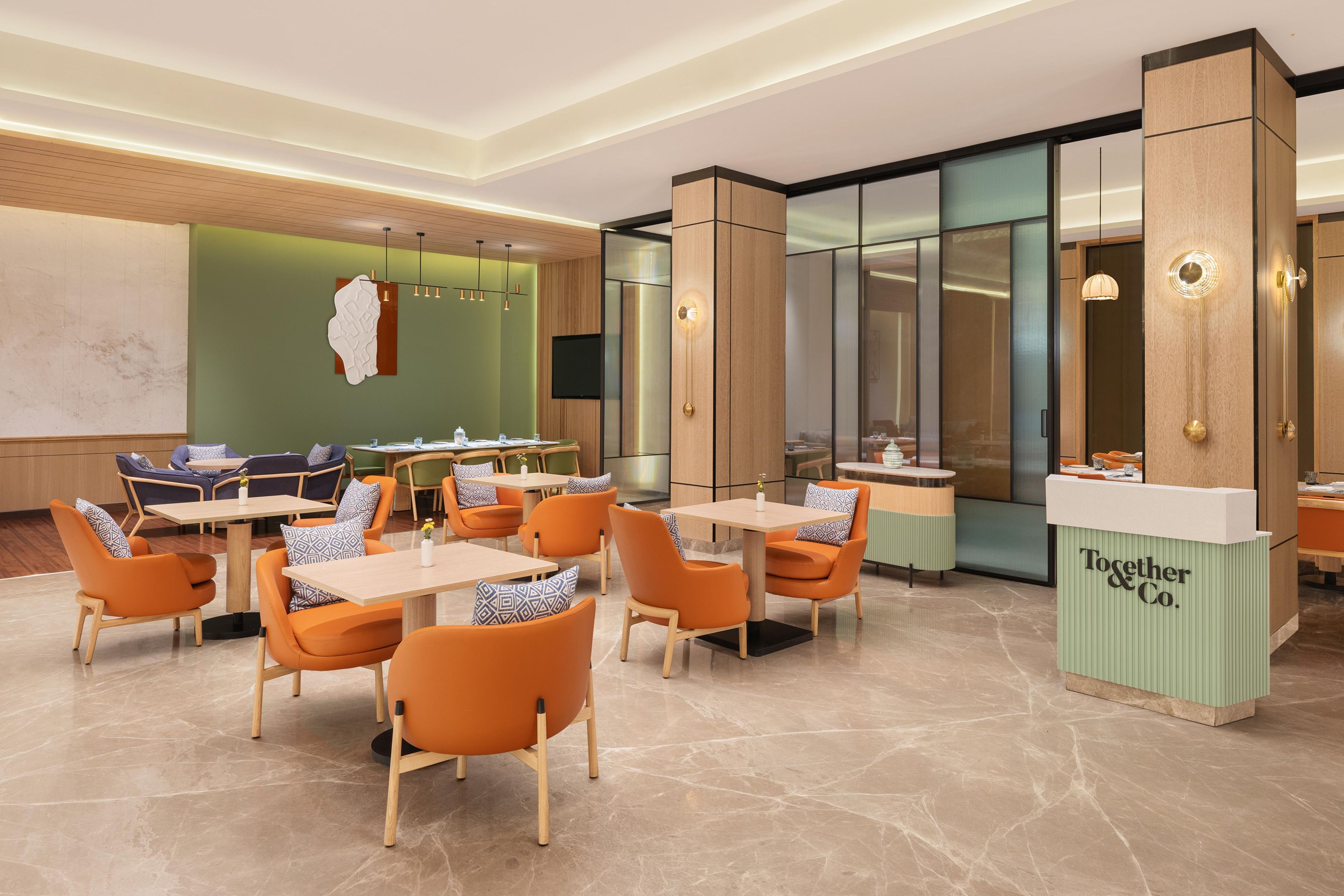 Un moderno vestíbulo de hotel con zonas de estar, un mostrador de recepción y una gran obra de arte abstracta en la pared.
