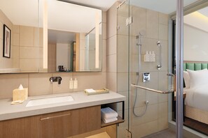 Une salle de bain moderne avec une douche à parois de verre, un lavabo avec un miroir et une table de chevet avec des articles de toilette.