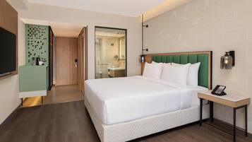 Una habitación de hotel con una cama grande, una mesita de noche con un teléfono, un cabecero verde y un espejo.