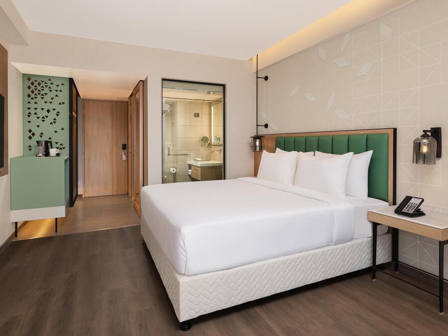 Una habitación de hotel con una cama grande, una mesita de noche con un teléfono, un cabecero verde y un espejo.