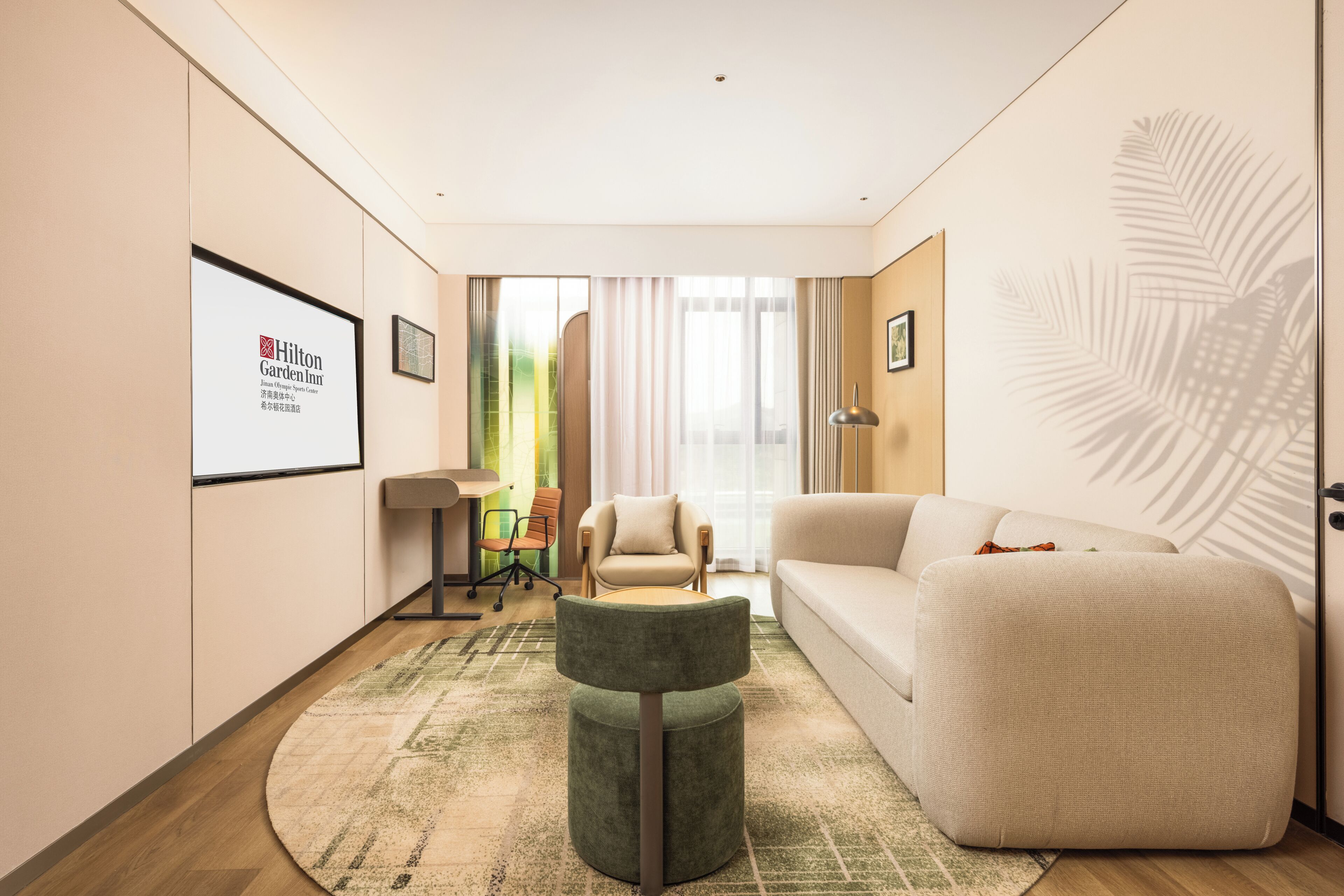A modern hotel room with a large window, a sofa, a round table, and a chair.