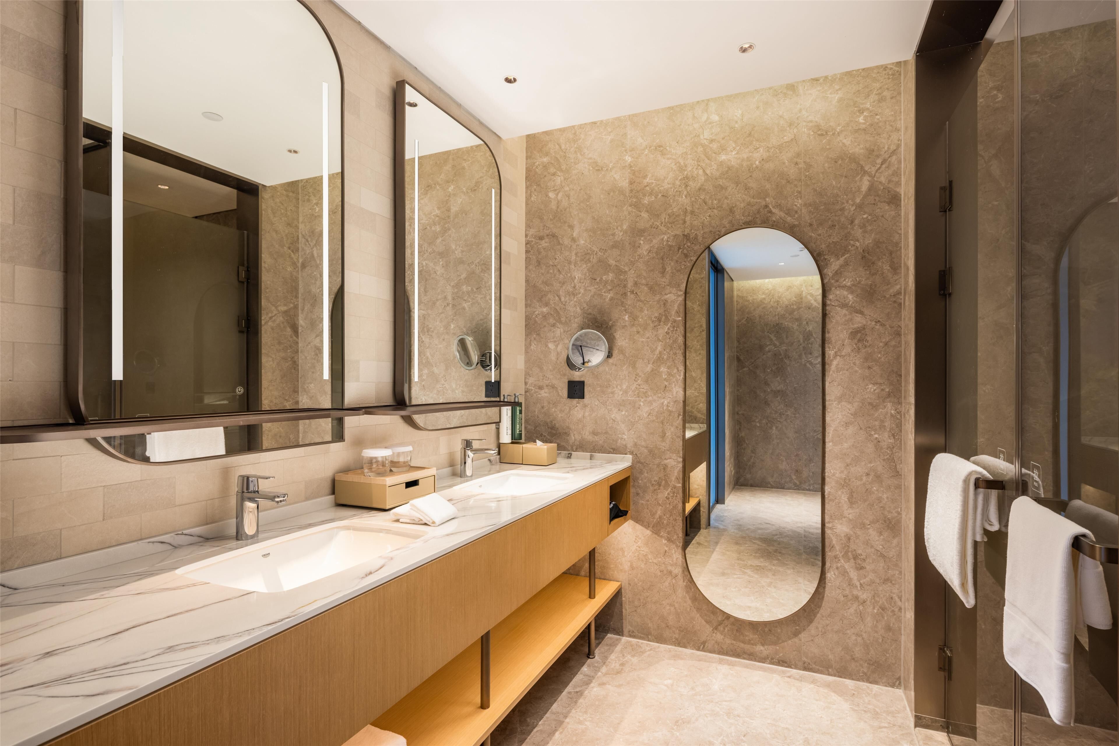 A modern bathroom with a marble sink, large mirrors, and a glass shower enclosure.