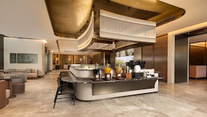Un moderno vestíbulo de hotel con una zona de bar central, espacios de esparcimiento y un techo alto con un diseño único.