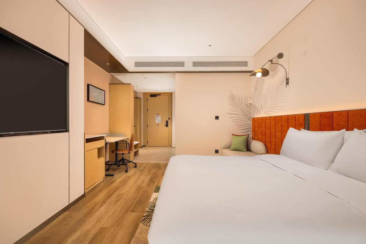 Una habitación de hotel con cama, escritorio, silla y una pantalla grande en la pared.