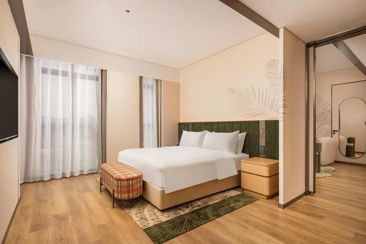 Una habitación de hotel moderna con una cama grande, una mesita de noche, una pequeña zona de estar y un espejo.