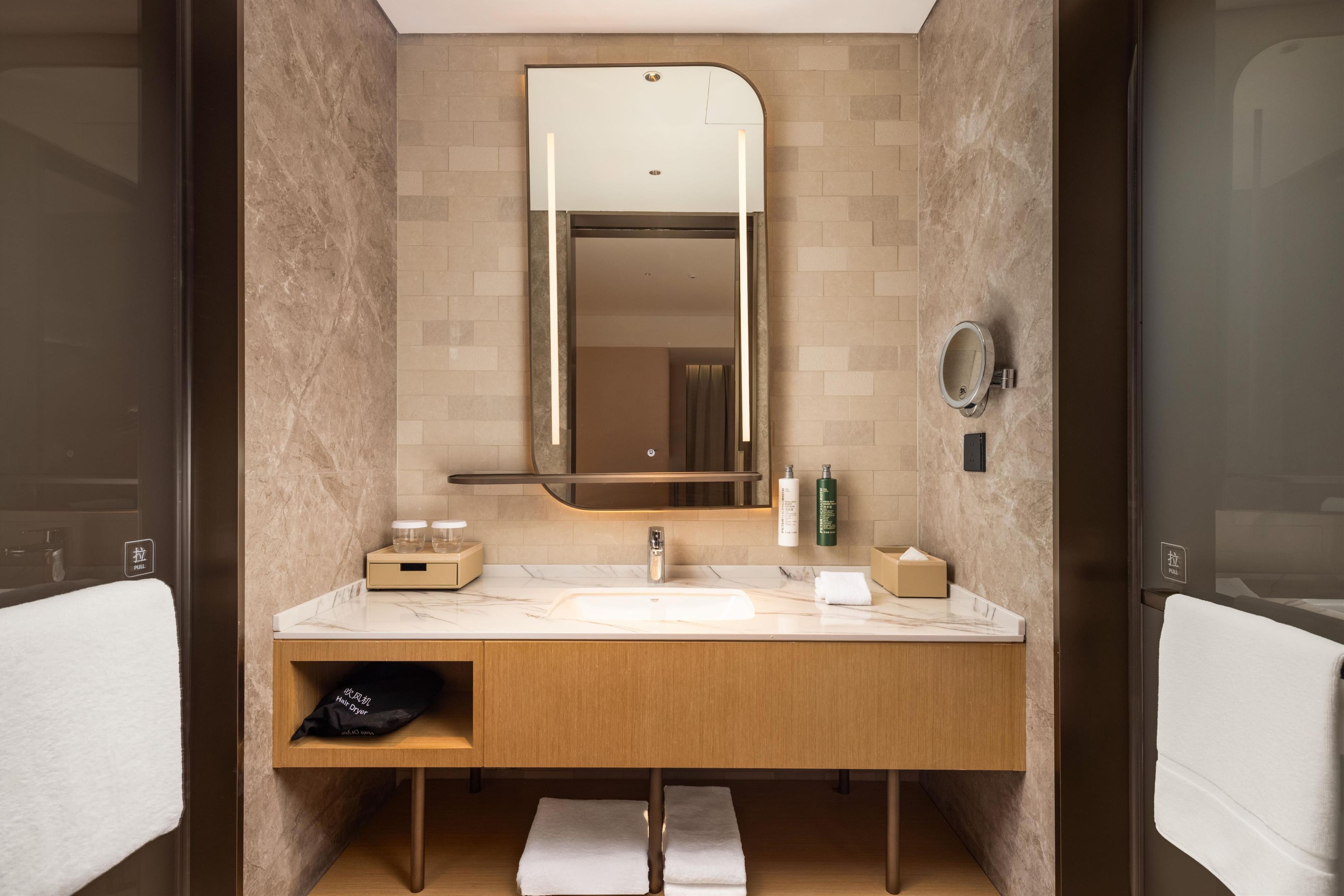 A modern bathroom with a marble vanity, a large mirror, and a towel rack.
