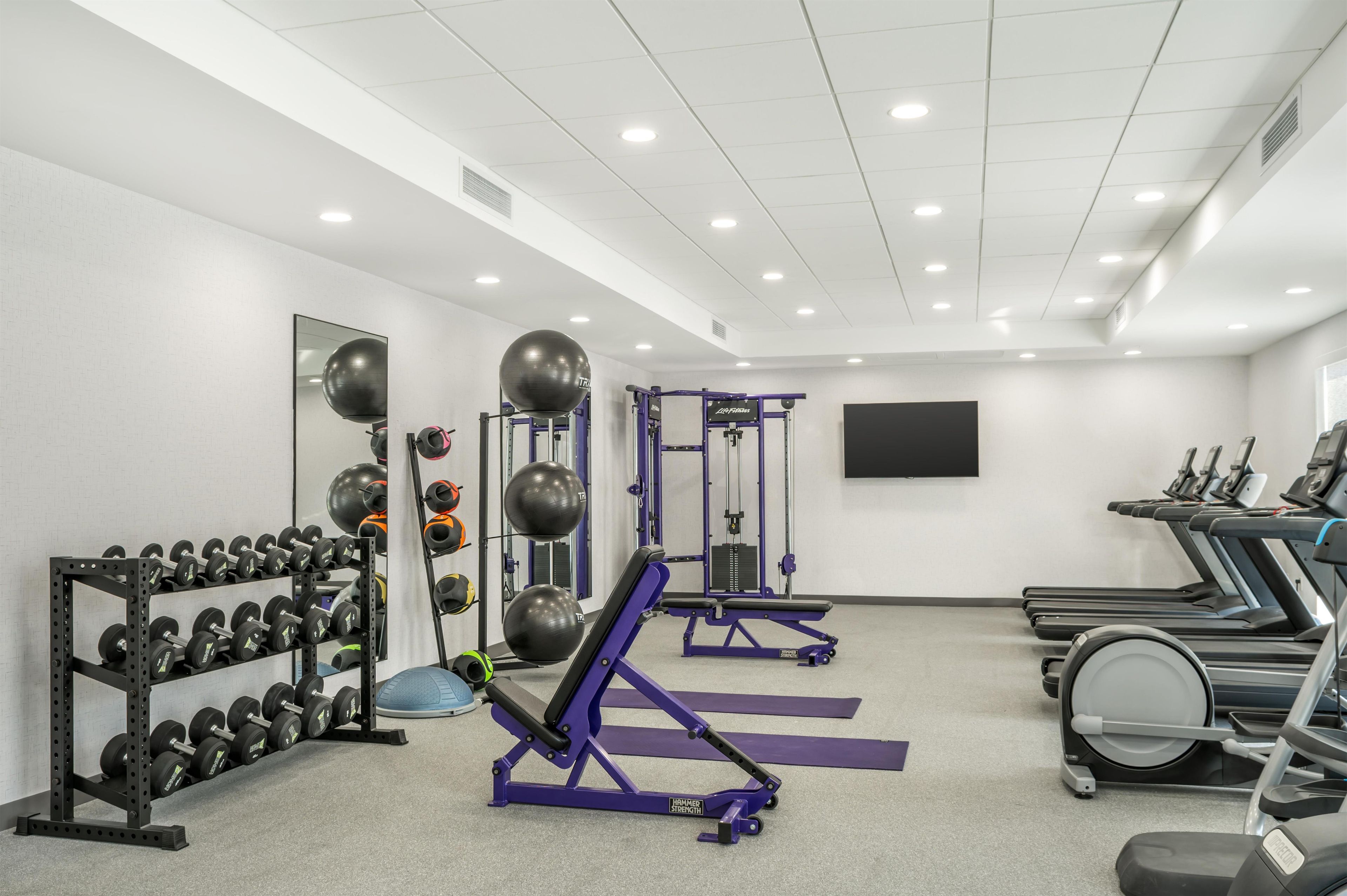 A gym with weight racks, exercise equipment, treadmills, and a large mirror.