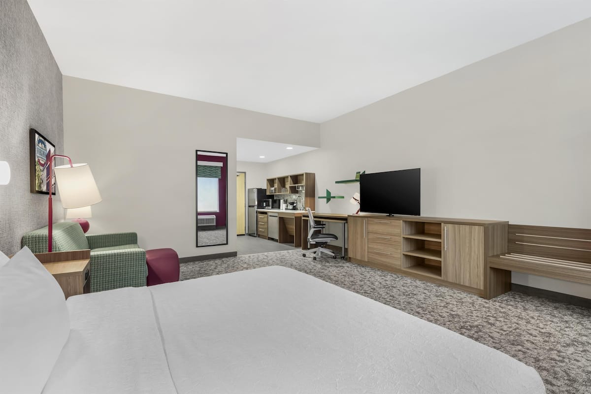 Een hotelkamer met een bed, bureau, stoel, televisie en een kleine kitchenette.