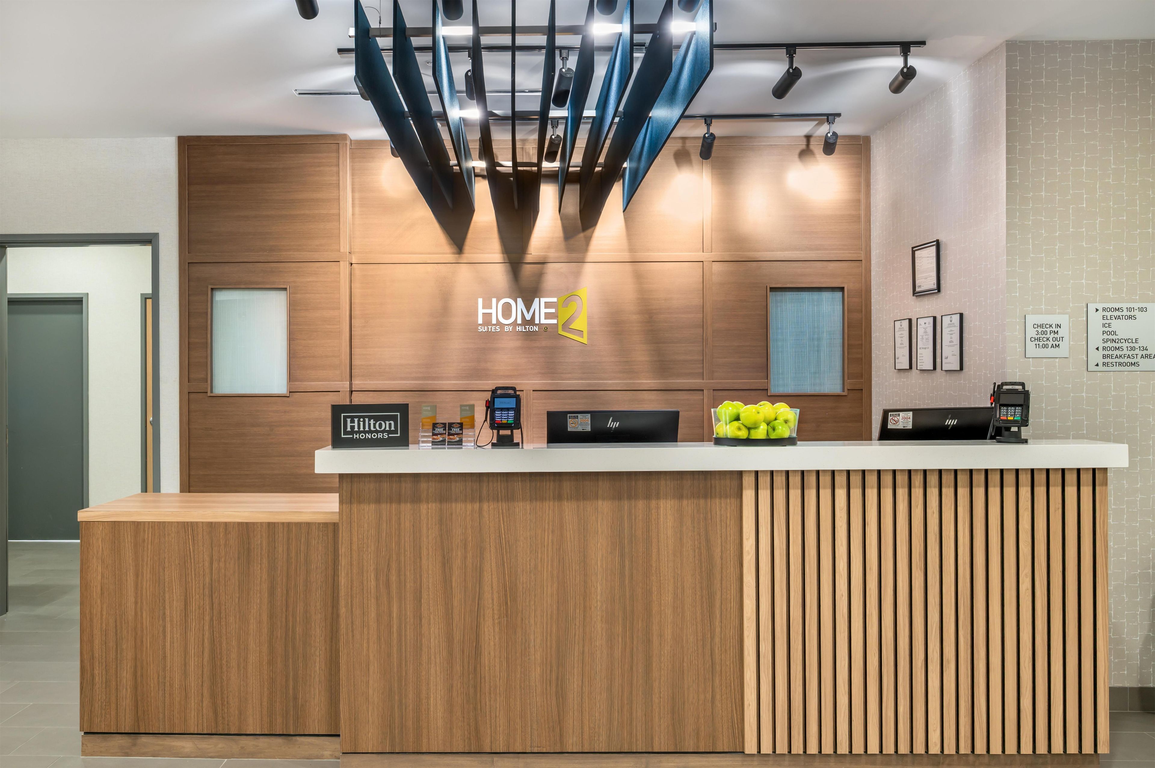 Un mostrador de recepción moderno en un hotel, con detalles de madera, una pantalla digital y un frutero.