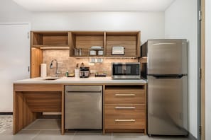 A compact kitchen with a built-in dishwasher, a stainless steel refrigerator, a microwave, and wooden cabinetry. - Home2 Suites By Hilton Harrisonburg University (Harrisonburg)