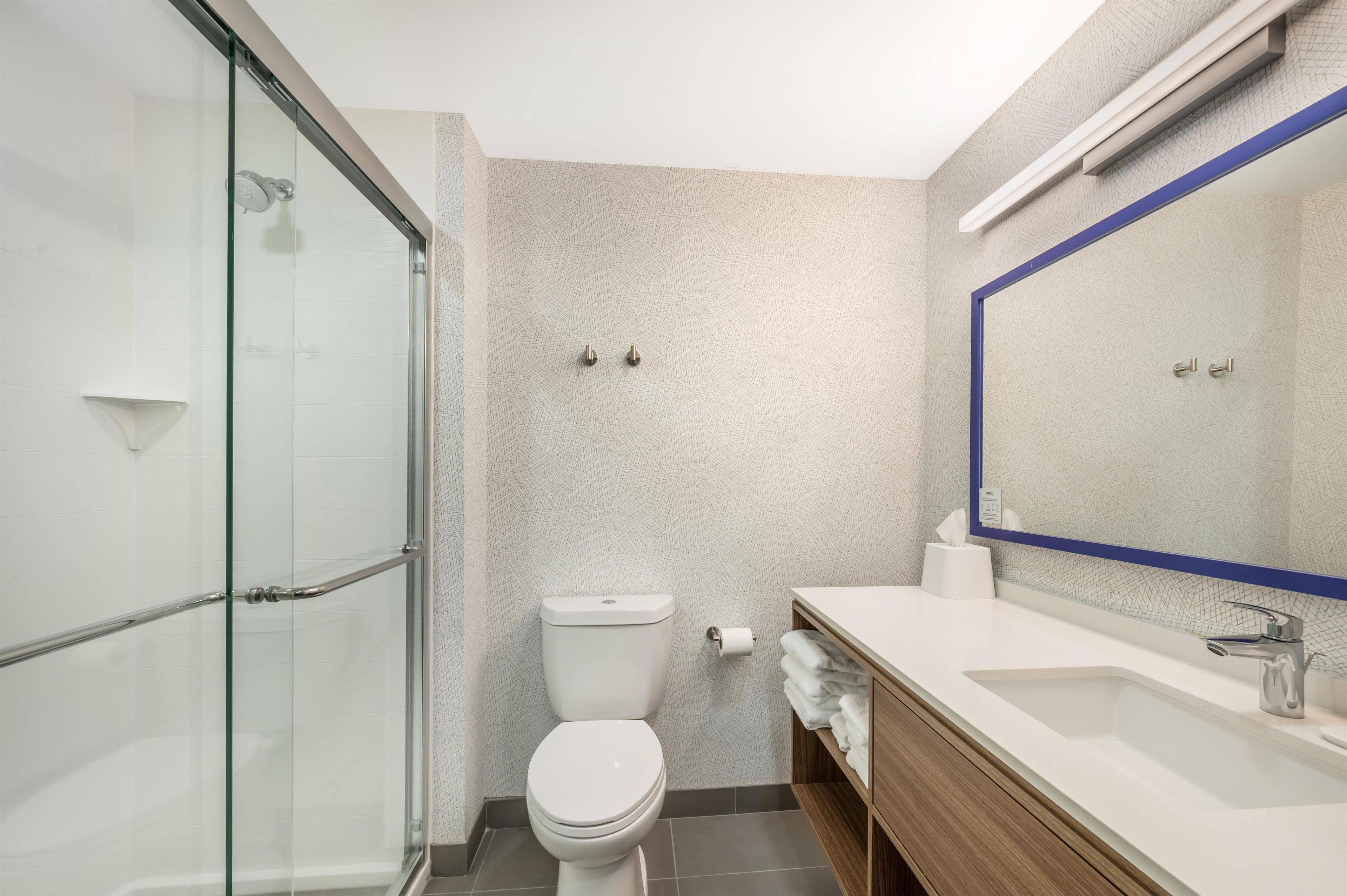 Une salle de bain moderne avec une douche à parois de verre, des toilettes, un lavabo avec un miroir et un porte-serviettes.