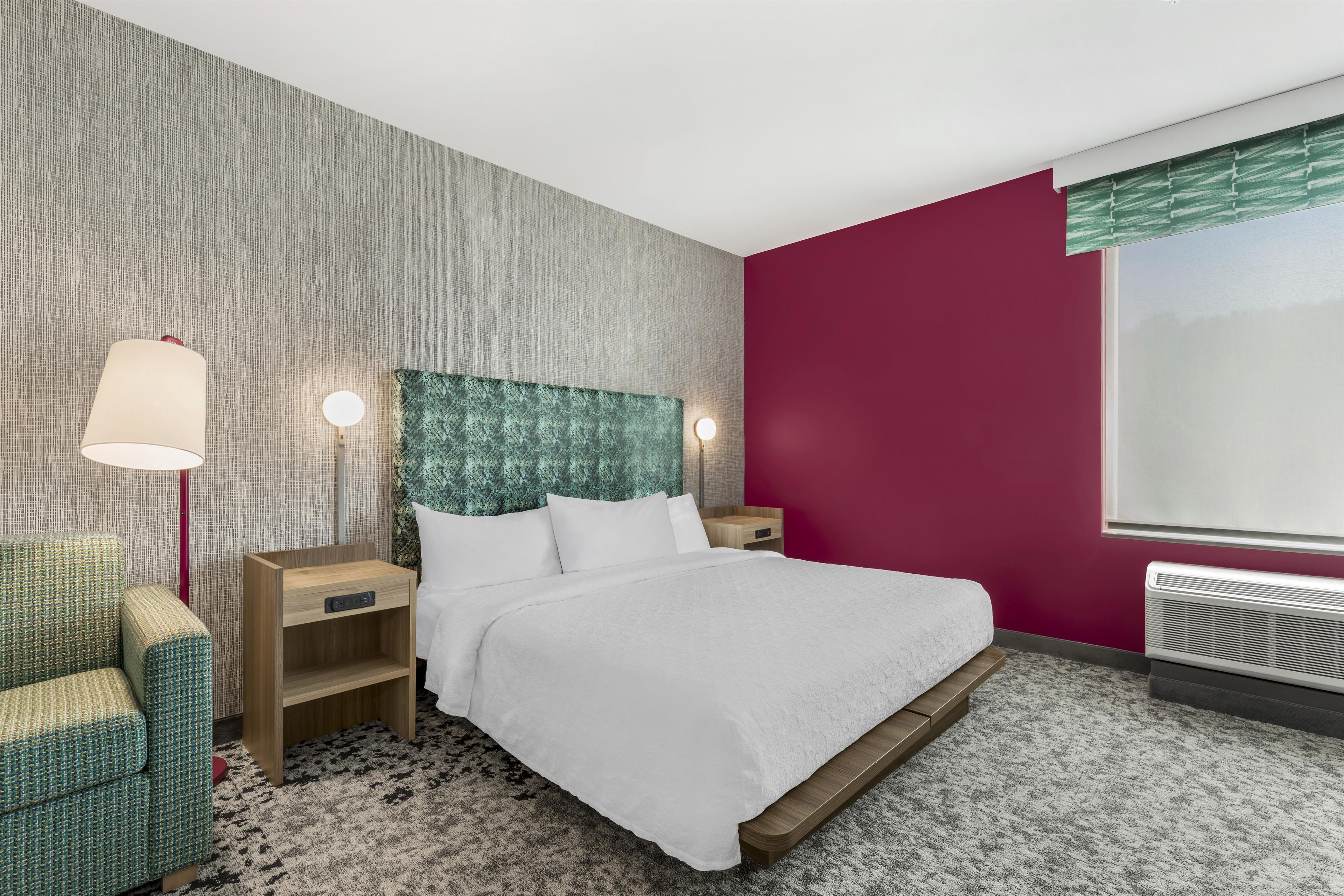 A hotel room with a bed, nightstands, a lamp, a chair, and a window.