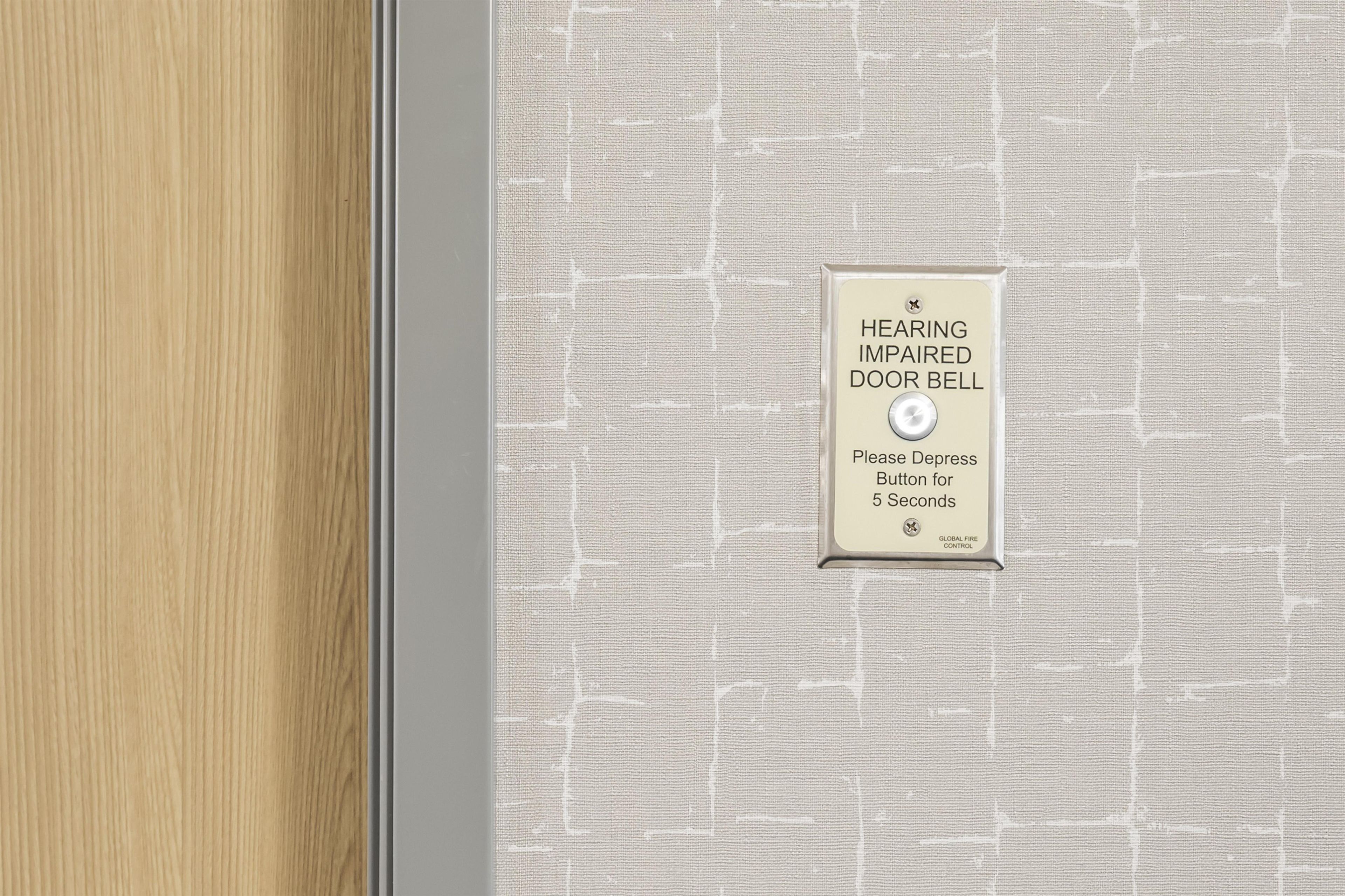A wall-mounted sign with a hearing impaired doorbell, a request to depress the button for 5 seconds, and a global fire control symbol.