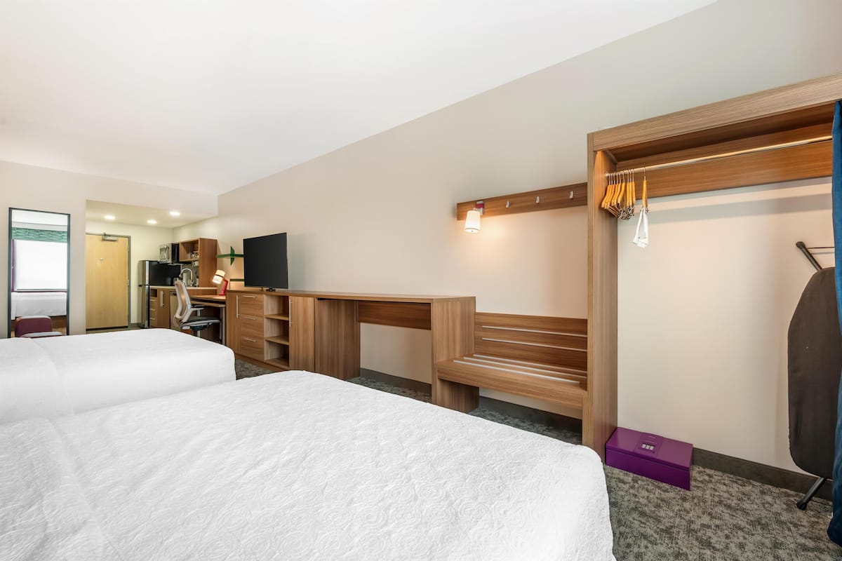 Een hotelkamer met twee bedden, een bureau, een televisie, een kledingkast en een badkamer op de achtergrond.