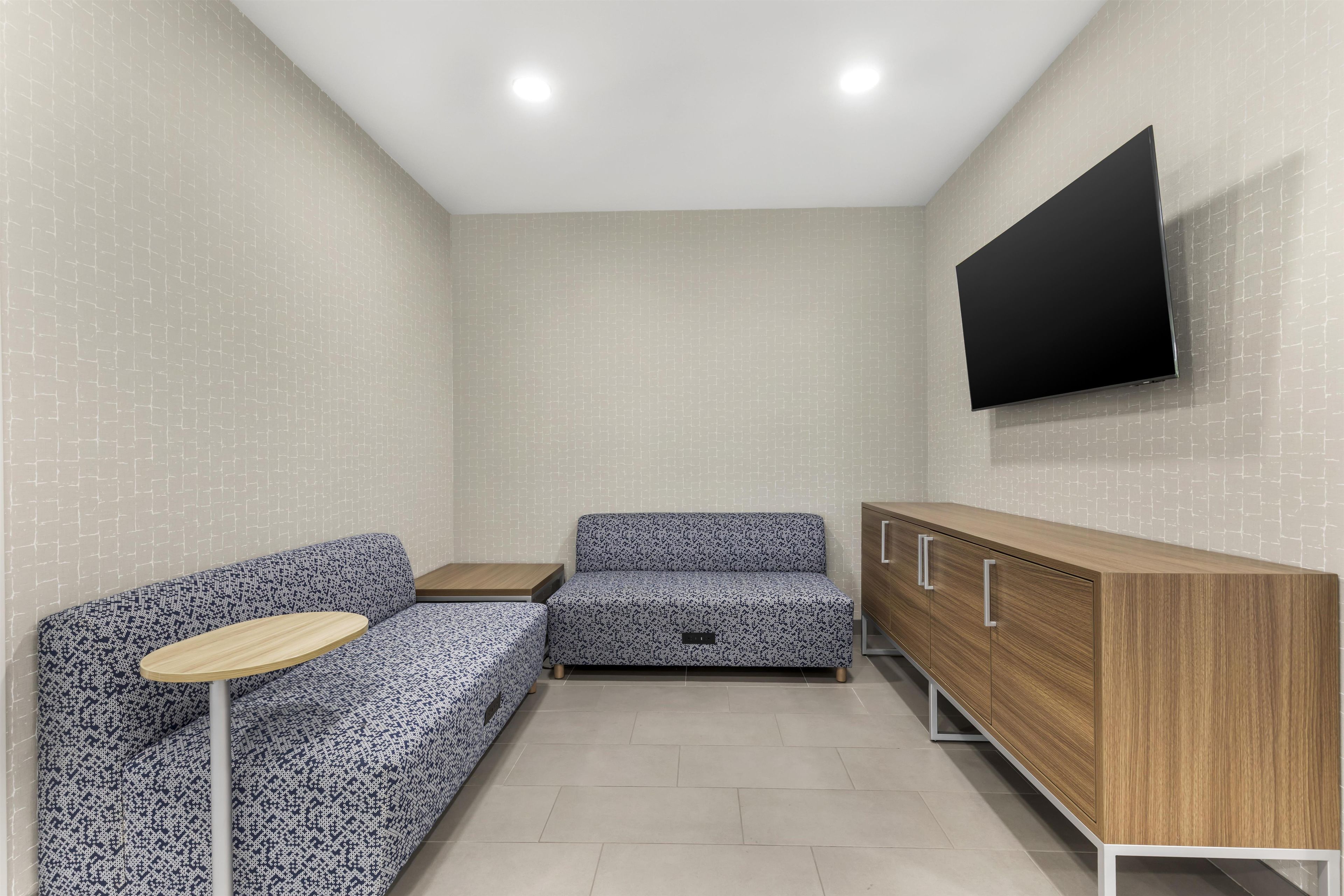 A modern room with a sofa, a small table, a cabinet, and a flat-screen TV mounted on the wall.