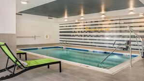 An indoor swimming pool with a tiled wall, a ladder, and a lounge chair. - Home2 Suites By Hilton Harrisonburg University (Harrisonburg)