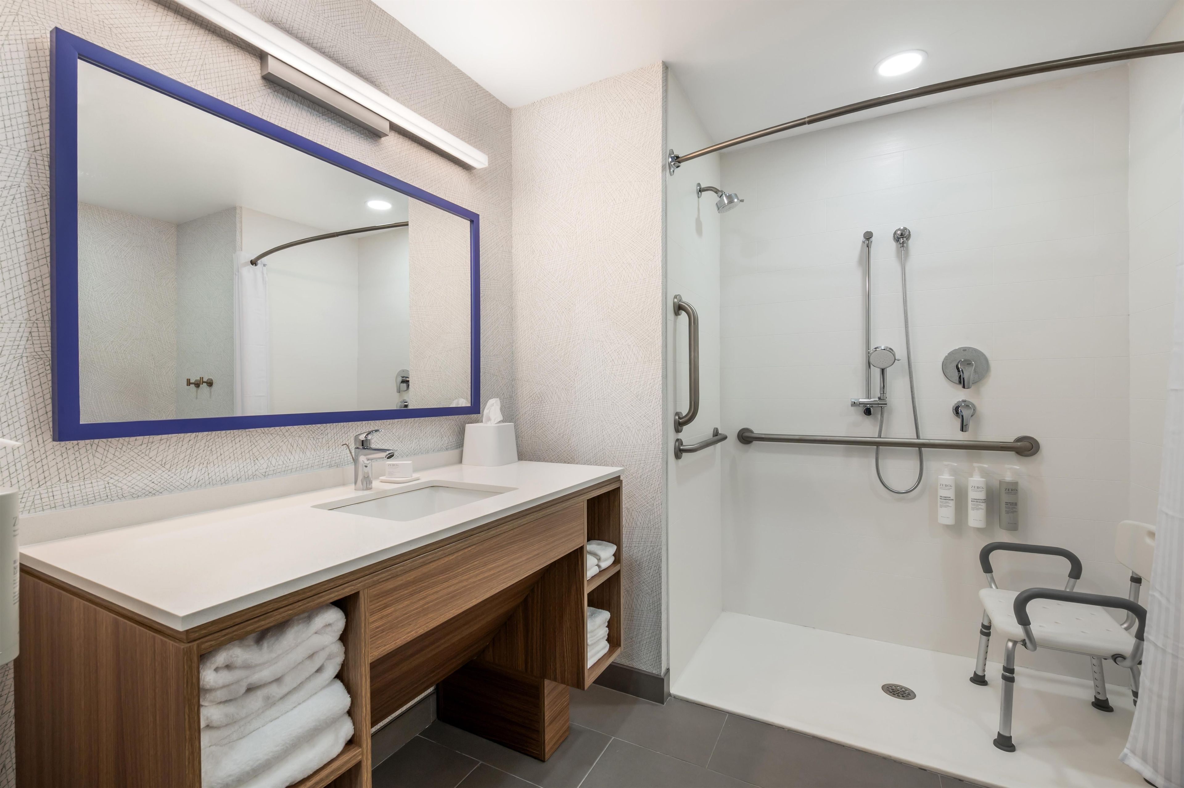 Een moderne badkamer met een grote spiegel, een douche met glazen deur en een wastafelmeubel met wastafel en handdoekopbergruimte.
