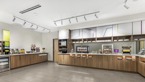 Une cuisine moderne avec des meubles en bois, une machine à café intégrée et une présentation de divers produits alimentaires.
