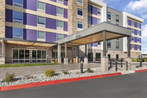 Un hotel de varios pisos con entrada cubierta, fachada de piedra y zona de estacionamiento.